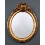 A decorative gilt oval wall mirror with scrolling crest flanked by fruiting swags to either side,