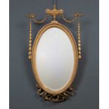 An antique gilt oval wall mirror with urn crest and ribbon tied husk swags, 40cm wide x 77cm