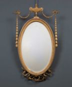 An antique gilt oval wall mirror with urn crest and ribbon tied husk swags, 40cm wide x 77cm