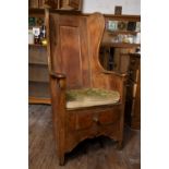 An early 19th century pine lambing chair, with panelled tall wing back, curved arms and solid