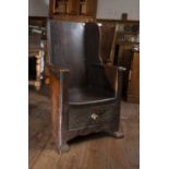 An 18th century oak and stained pine lambing chair, with wing back, curved arms and solid seat,
