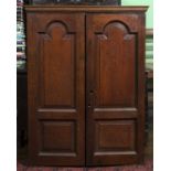 An 18th century oak small cupboard, having a pair of arch panelled doors enclosing shelves and