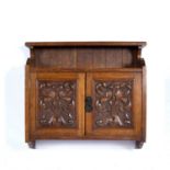 In the manner of Heals oak twin door cabinet, with carved foliate decoration and fitted drawers to