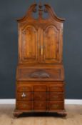 A walnut continental style bureau cabinet with arching panel doors beneath a swan neck crest with