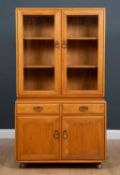 An Ercol light elm cabinet with twin glazed doors above two short drawers and two cupboard doors, on