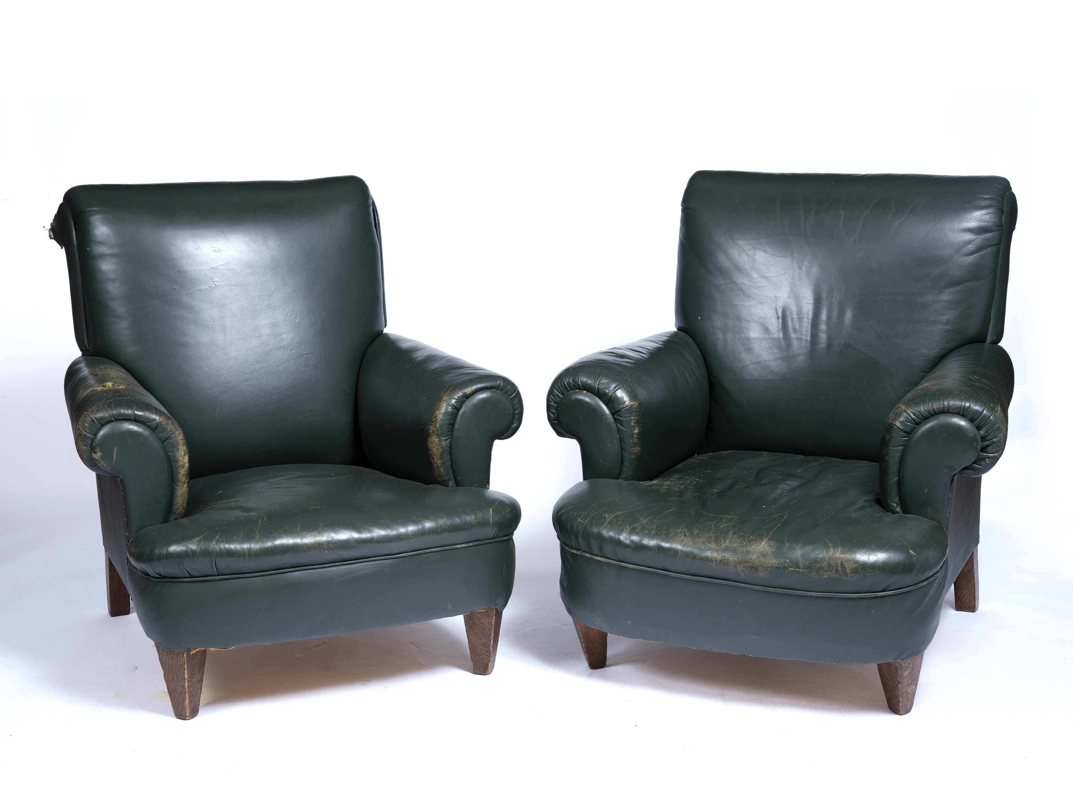 A matched pair of early 20th century library armchairs upholstered in green leather with rolled