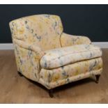 A Howard style deep armchair standing on turned tapering front legs and brass casters, 84cm wide x
