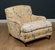 A Howard style deep armchair standing on turned tapering front legs and brass casters, 84cm wide x