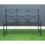 A three-seater black painted metal garden bench, with strap metal seat and arching cut out back
