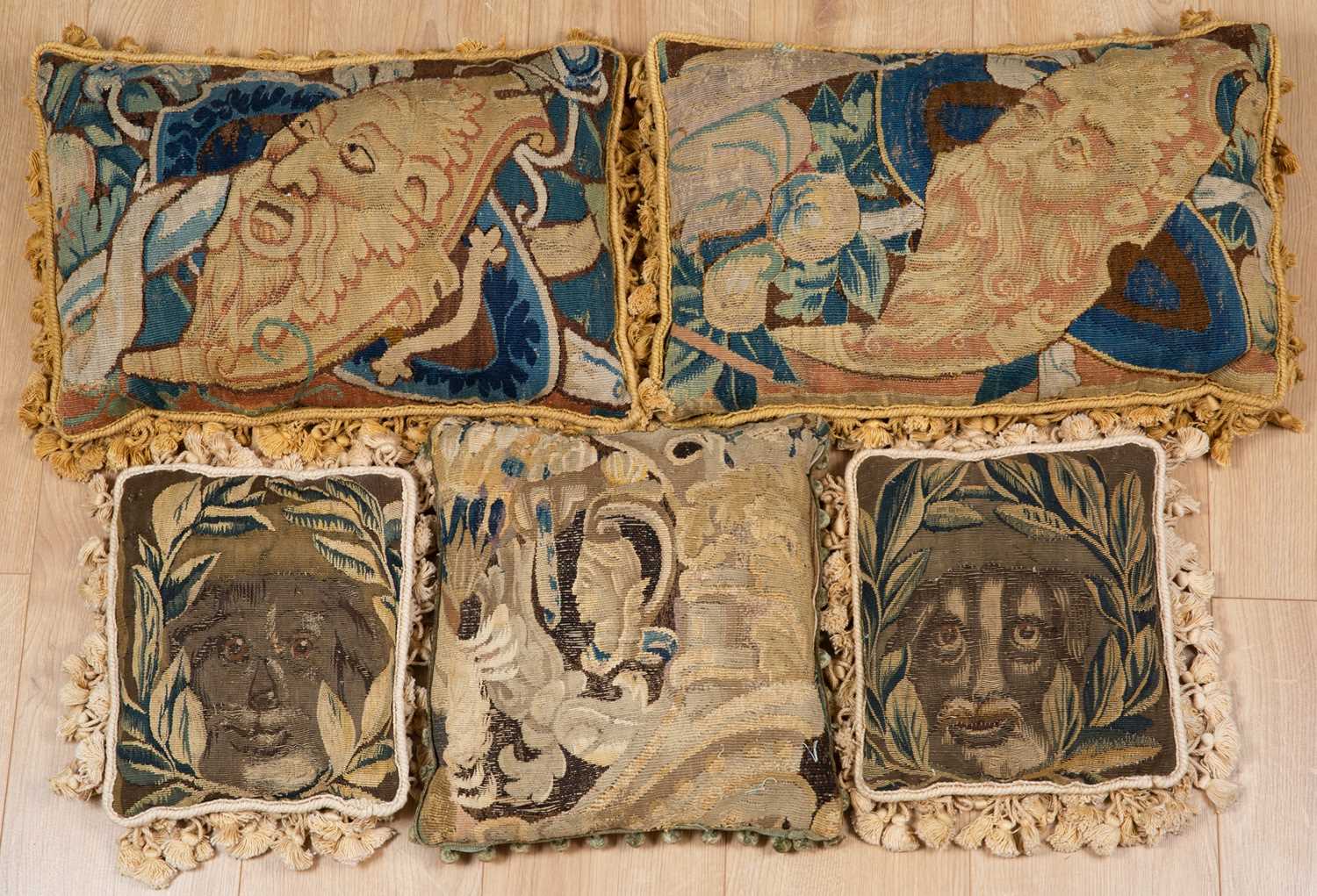 A pair of 17th century tapestry fragments used as cushions, each decorated with bearded masks and