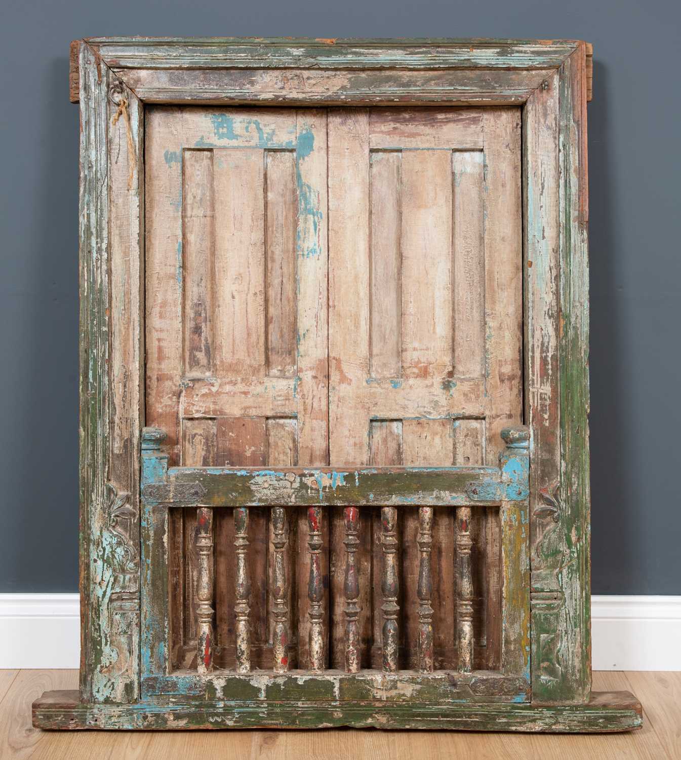 An antique Rajastani painted hardwood window frame with panelled shutters and turned supports to the