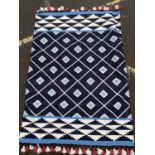 A tribal flat weave rug with black and white diamonds and coloured tassels, originally retailed by