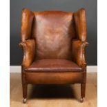 A Georgian style brown leather upholstered wing back armchair with square tapering front legs and