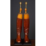 A pair of decorative table lamps constructed from brown leather riding boots, mounted on rectangular