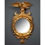 A giltwood carved convex circular wall mirror, with eagle on scrolled pedestal crest, foliate