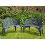 A pair of green painted cast iron garden benches with mask terminals to the arms, the backs with