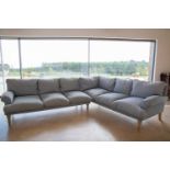 A light blue upholstered L shaped six seater sofa standing on turned tapering oak front legs, with