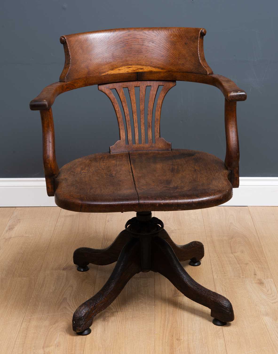 An Edwardian oak swivel desk chair with open arms on outswept supports, 58cm wide x 52cm deep.