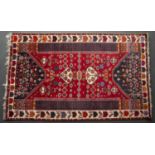 A Middle Eastern red ground rug with polychrome geometric decoration and a banded border, 234cm x