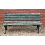 A green painted curved back wooden and cast iron garden bench, the bracket supports with scrolling
