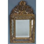 A bronze repousse cushion frame wall mirror, cartouche topped with bevelled facets on a pitch pine