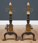 A pair of Victorian brass and cast iron fire dogs, with embossed fleur-de-lis form finials on curved