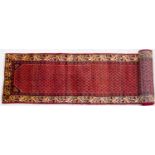 A Middle Eastern Araak woollen runner with central red ground and a cream border, 480cm x