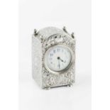 A late Victorian silver small carriage timepiece, the arched case embossed with scrolling foliage,