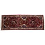 Small red ground runner with allover trailing foliate designs around two small medallions, 69cm x