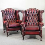A pair of red leather upholstered wing back armchairs