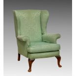 A Parker Knoll wingback armchair, upholstered in light green damask, with beechwood cabriole style