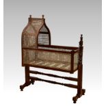 A Victorian caned mahogany swinging cot on stand, the caned cot with lancet shaped half-canopy and
