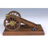 An early 20th century desk model of a cannon, having twin wooden spoked wheels, brass mounted