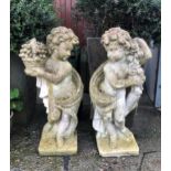 A pair of architectural composite stone garden putti statues, nicely weathered, one carrying a