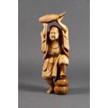 A Japanese carved ivory okimono, 19th century, of a man standing with one foot resting on a gourd-