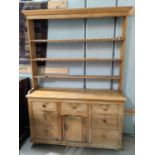 A Victorian stripped pine Welsh dresser with delft rack over 7 drawers and central cupboard, width