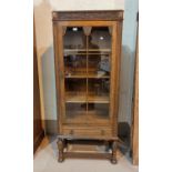 A 1930's golden oak display cabinet, tall and narrow, with carved decoration, single glazed door and