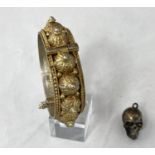 An unusual skull pendant containing miniature dice; a Middle Eastern hinged bangle in ornate white
