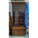 An Arts and Crafts style golden oak bookcase with 4 bulls' eye panes to the 2 glazed doors, double