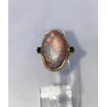 A yellow metal dress ring set large oval black opal coloured stone, flanked by 2 green stones,