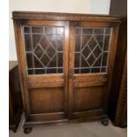 A Jacobean style oak side cabinet enclosed by 2 part leaded glass doors