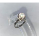 A white metal dress ring set with a pearl flanked by a small diamond to each shoulder, stamped '