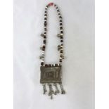 A Mid/Far Eastern white metal large pendant of filigree rectangular form, on variegated bead