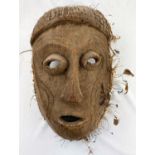 A large African tribal mask, carved snake decoration applied grass and feather border 41cm