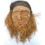 An African tribal mask with applied grass beard, woven grass and fabric head covering, 38cm