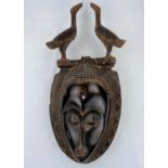 An African tribal carved and patinated wood mask with double bird headdress, shallow carved