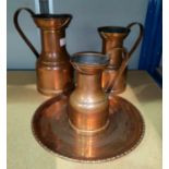 A graduating set of 3 copper jugs in the Arts & Crafts style; a copper circular tray