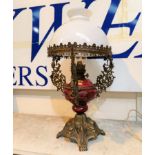 An ornate table oil lamp in red pottery and cast brass