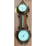 An Edwardian clock/barometer with thermometer in carved oak wall hanging case