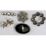 A circular silver floral brooch, a faceted clear stone brooch, two others and a pair of clip-on
